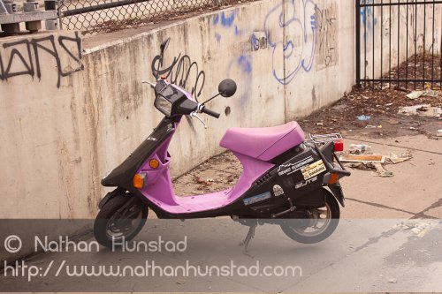 A purple scooter sits among trash on the sidewalk.